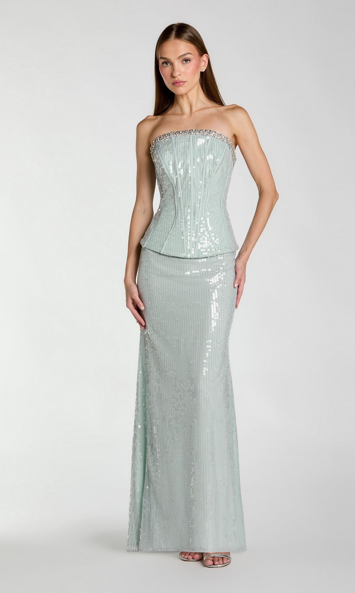A woman wearing the Mac Duggal 27776 long formal dress in pale blue, featuring a strapless sequin design with a fitted corset bodice and floor-length skirt, stands against a plain light background. This stunning gown is the perfect choice for sophisticated evening occasions.